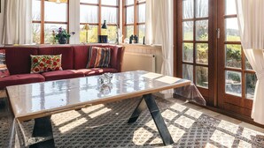 Un salon chaleureux avec un canapé rouge, une table basse en verre et de grandes fenêtres ornées de rideaux.