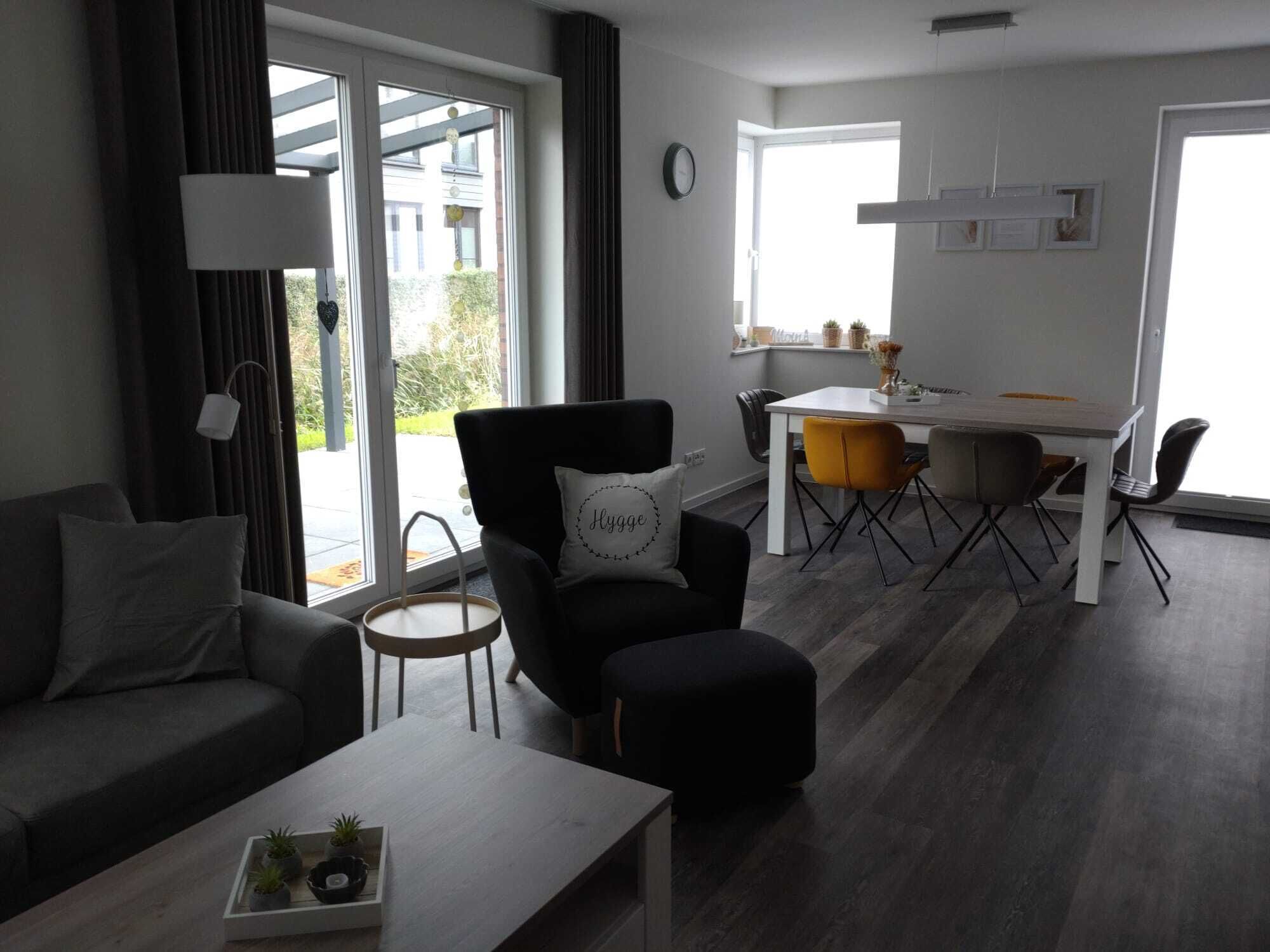 A modern living room with a sofa, a black armchair with a pillow, a coffee table, and a dining area with a table and chairs.