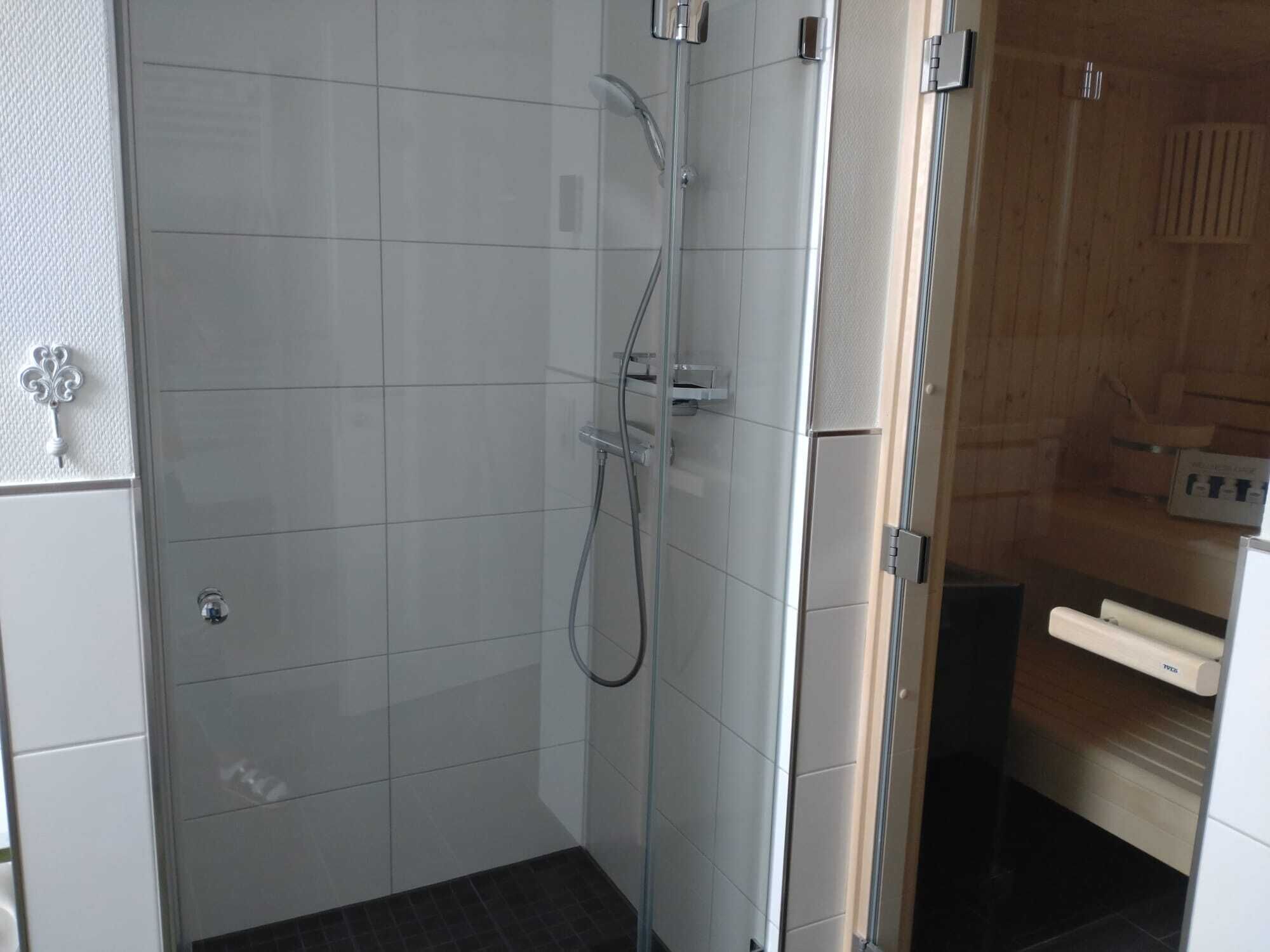 A modern bathroom with a glass shower enclosure, white tiled walls, and a wooden panel wall.