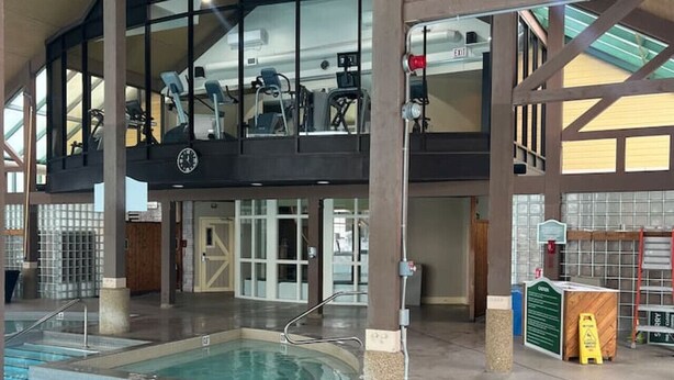 Una piscina interior con un entrepiso, equipo de gimnasia y un reloj a la vista.
