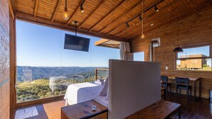 A wooden cabin with a large window offering a mountain view, a bed, a TV, and a dining area.