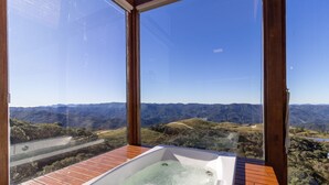 A hot tub with a wooden deck and a view of a mountainous landscape through large windows.