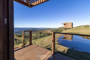 A wooden deck with a view of a hill and a small building. - Cabana com vista panorâmica VST006 (Anitápolis)