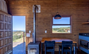 Interior de uma cabana de madeira com uma janela grande, um fogão e uma área de jantar com cadeiras.