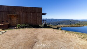 A wooden building with a door and steps leading to a deck, overlooking a lake and mountains.