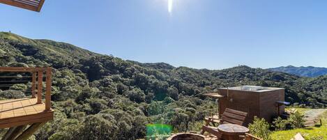 A wooden deck with a brick fire pit and seating, overlooking a lush valley and mountains.