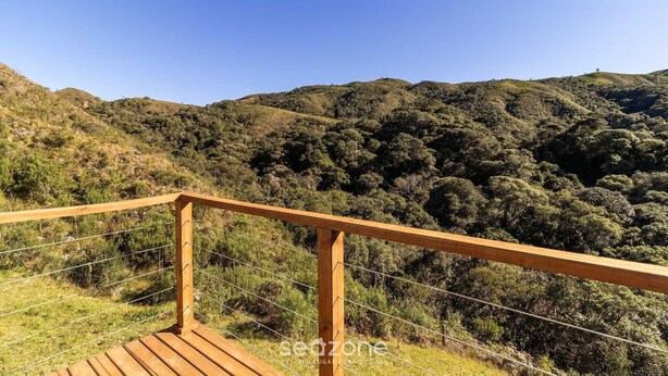 A wooden deck with a metal railing overlooking a hilly landscape with dense greenery. - Cabana vista deslumbrante serra VST020 (Anitápolis)