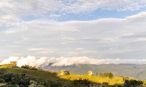 A mountainous landscape with two small buildings on a grassy hill. - Cabana vista deslumbrante serra VST020 (Anitápolis)