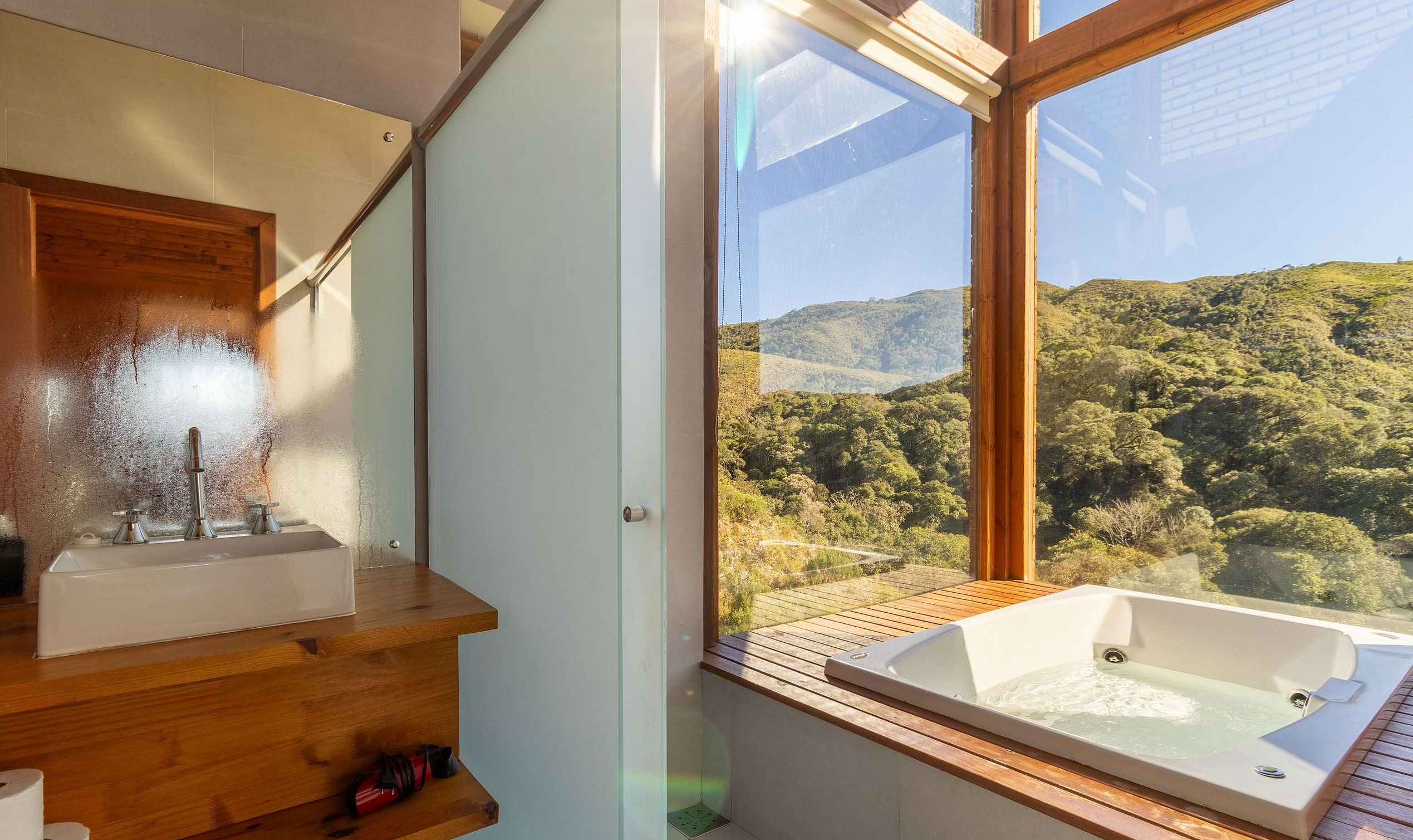 A bathroom with a wooden vanity, a sink, and a large window offering a view of a forested hillside.