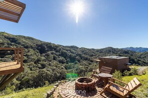 Una terraza de madera con un hogar a leña de ladrillo y asientos, con vistas a un valle exuberante y montañas.