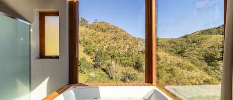 A modern bathroom with a hot tub, large windows, and a view of a hilly landscape.