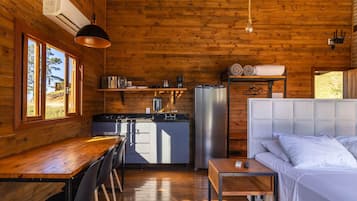Interior de una cabaña de madera con cocina, comedor y una cama.