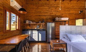 A wooden cabin interior with a kitchen, dining area, and a bed. - Cabana vista deslumbrante serra VST020 (Anitápolis)