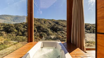 A hot tub on a wooden deck with a view of a forested hillside.