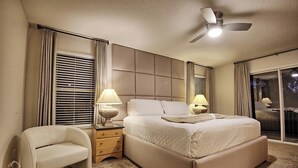 Un dormitorio con una cama grande, una mesita de noche con lámparas, una silla y un ventilador de techo.