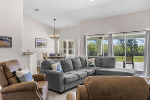 A modern living room with a grey sectional sofa, brown armchairs, and a dining area with a table and chairs. - Garden view retreat w/ balcony & BBQ grill (Merritt Island)