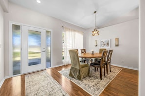 A dining area with a wooden table and chairs, a chandelier, and a view through frosted glass doors. - Garden view retreat w/ balcony & BBQ grill (Merritt Island)