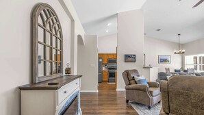 Ein geräumiges Wohnzimmer mit Kamin, im Hintergrund eine Küche und ein Essbereich mit einer Kronleuchter.