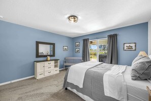 A bedroom with a bed, a dresser, a bench, and a window with curtains.