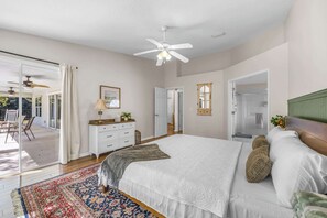 Une chambre spacieuse avec un grand lit, un ventilateur de plafond et une vue sur l’extérieur grâce à une porte-fenêtre coulissante.