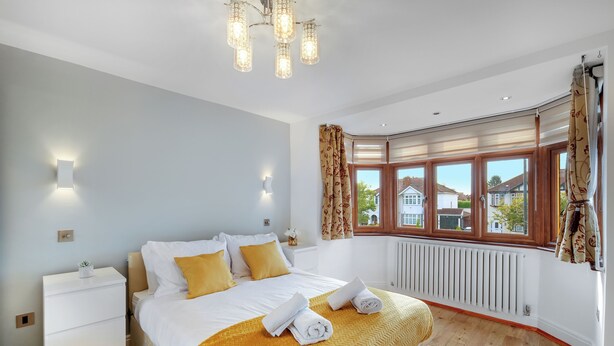 A bedroom with a bed, bedside tables, a radiator, and a window with curtains. - Spacious & Cosy 3 bedroom house (Enfield)