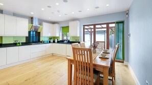 A modern kitchen with white cabinets, a wooden dining table, and recessed ceiling lights. - Spacious & Cosy 3 bedroom house (Enfield)