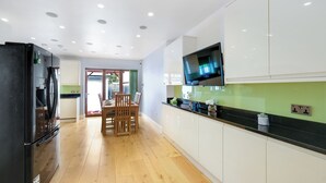 A modern kitchen with a black refrigerator, white cabinets, a black countertop, and a flat-screen TV mounted above the counter. - Spacious & Cosy 3 bedroom house (Enfield)