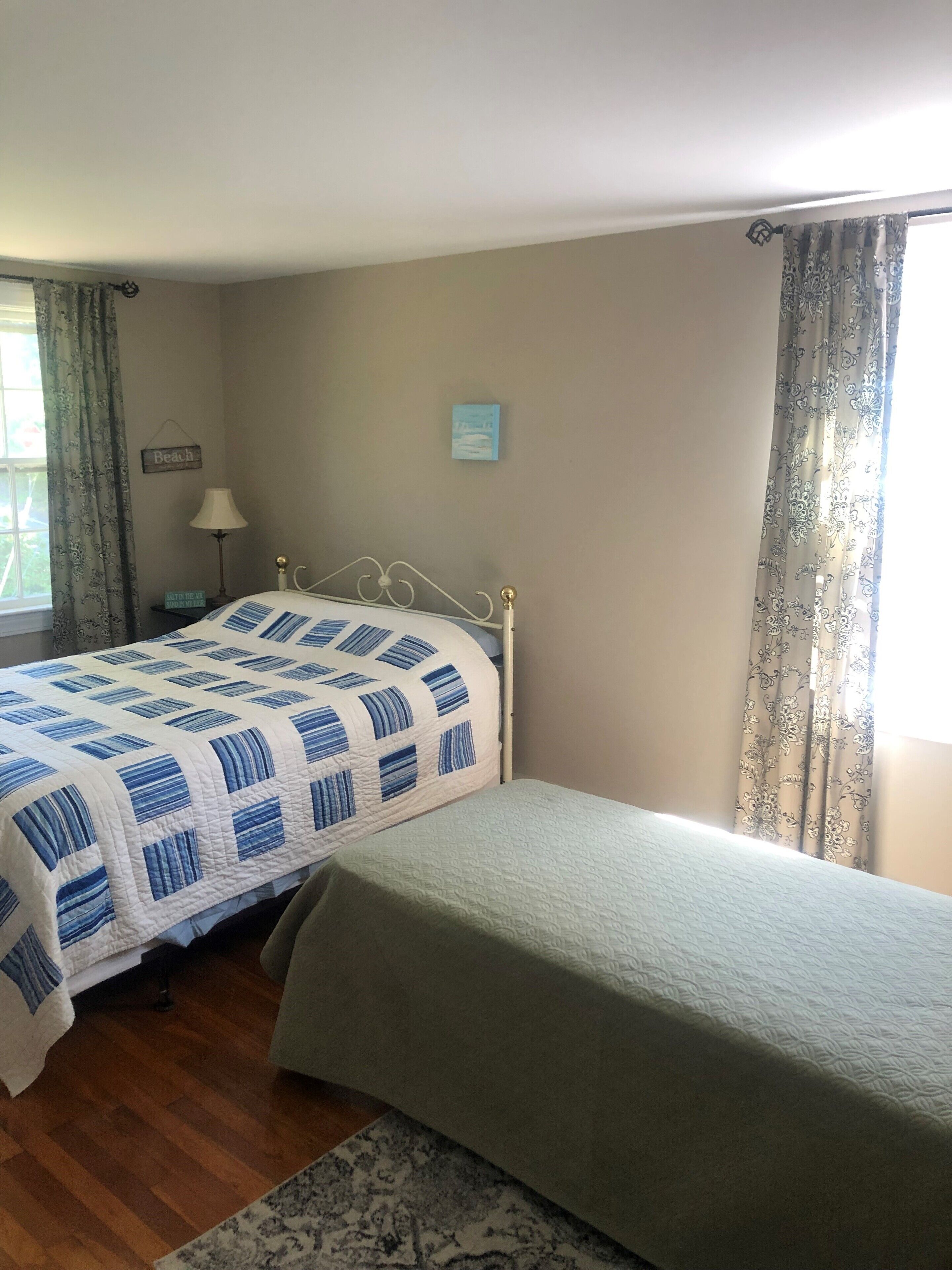 A bedroom with a bed, a nightstand, a lamp, a small picture, and a window with curtains.