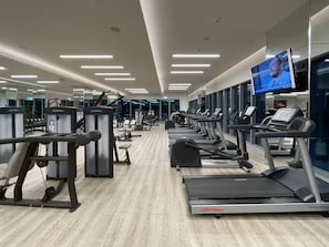 Ginásio com esteiras, máquinas de musculação e uma tela de TV.