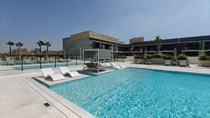 A rooftop pool with lounge chairs and umbrellas, surrounded by modern buildings.