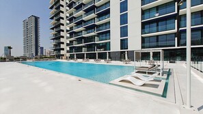 Um edifício moderno com piscina no terraço, várias varandas e vista clara para o horizonte da cidade.