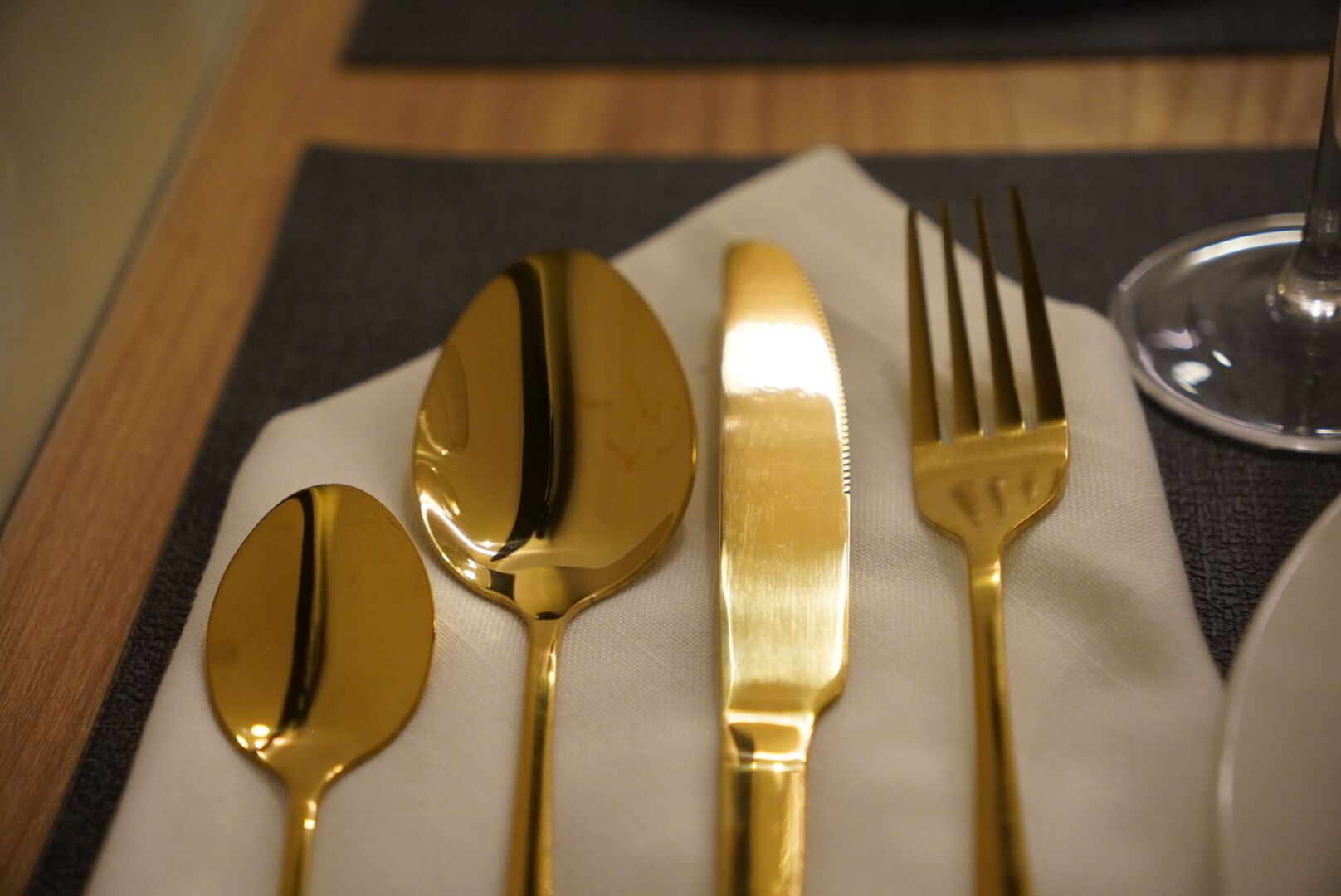 A table setting with a napkin, a spoon, a knife, a fork, and a glass.