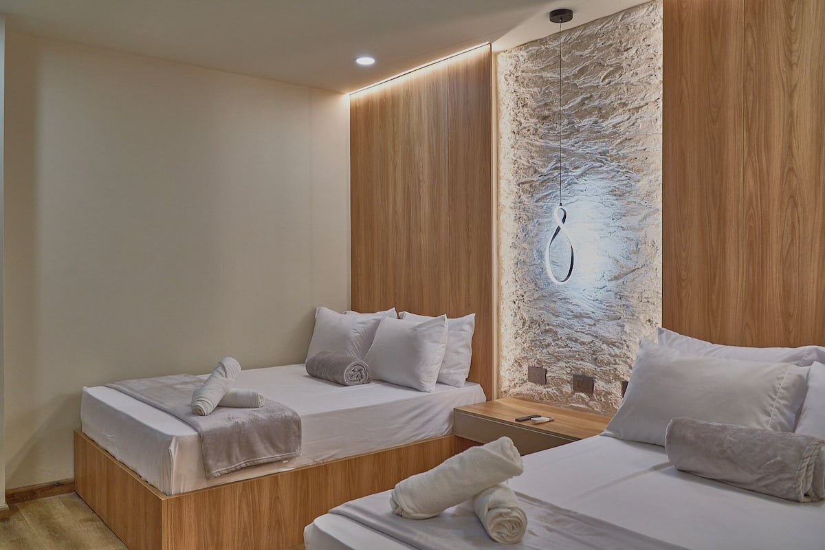 A modern hotel room with two beds, wooden headboards, and a textured stone accent wall.