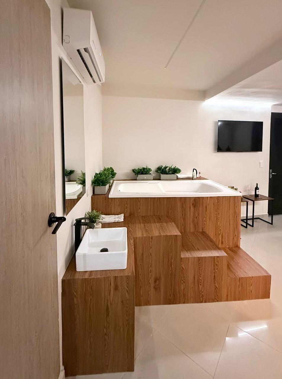 A modern bathroom with a wooden vanity, a sink, a large mirror, and a built-in bathtub.