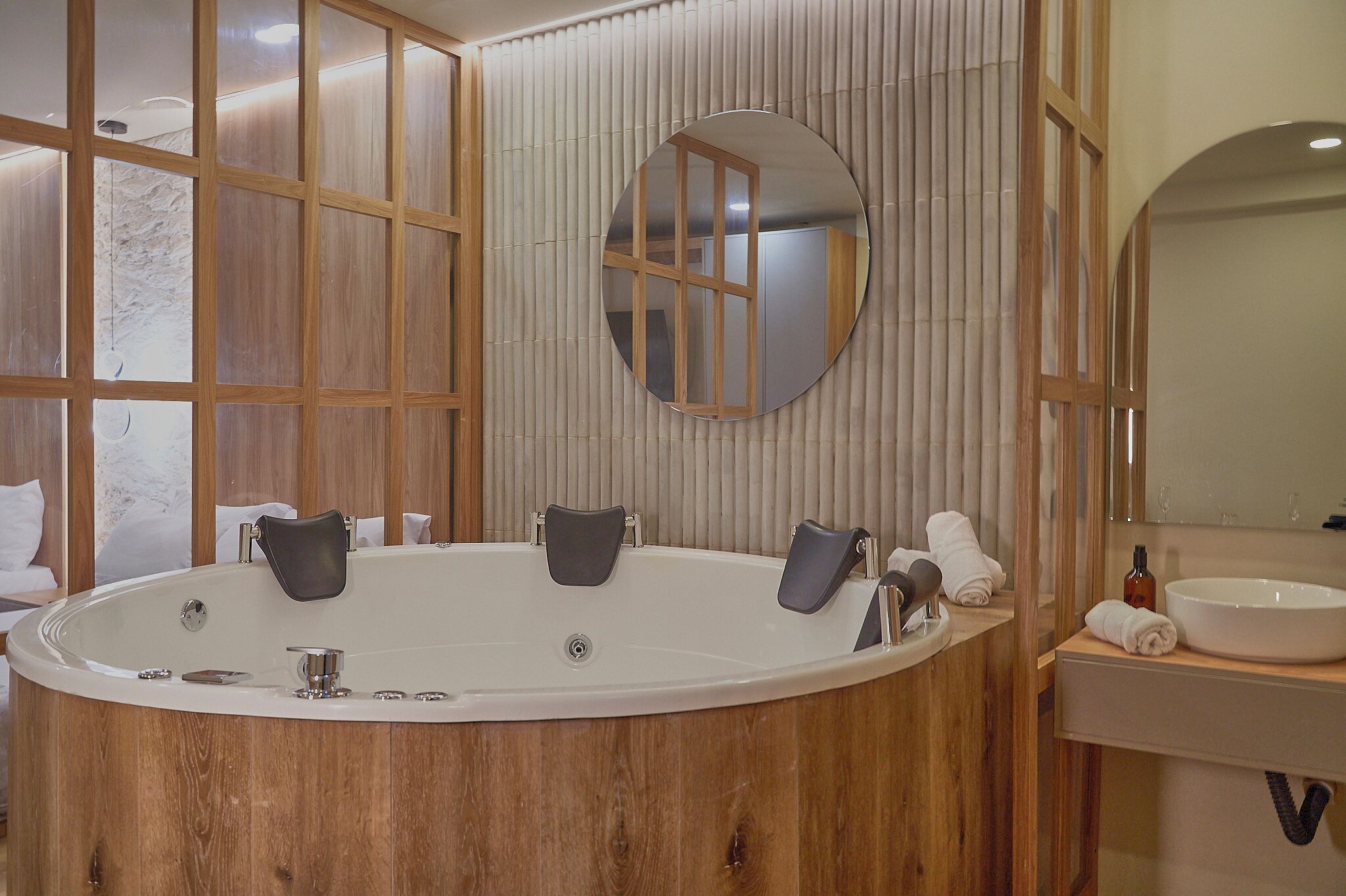 Une salle de bain moderne avec une grande baignoire ovale, un lambris en bois, un miroir rond et un lavabo blanc.