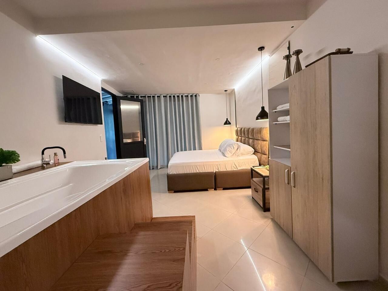 Un dormitorio moderno con una cama grande, mesitas de noche, un armario y un baño con bañera y lavabo.