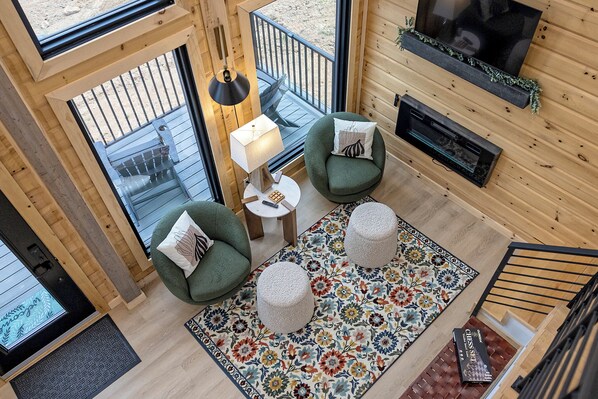 A cozy room with two green armchairs, a small table with a lamp, a colorful rug, and a TV mounted on the wall. - The Fives - 22450 Cloud View Luxury Japandi Cabin (Bristol)