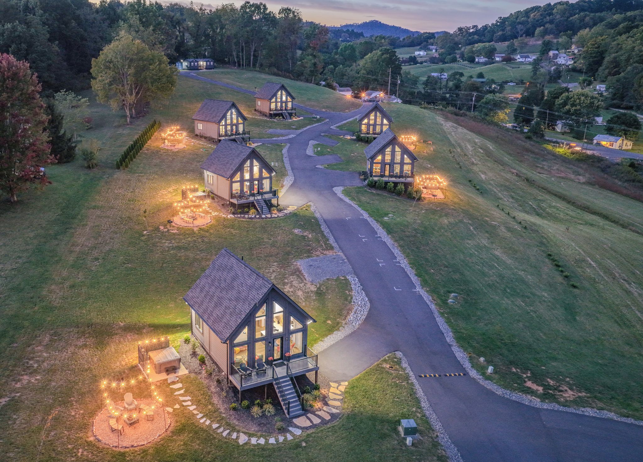 Un conjunto de cabañas modernas con ventanas amplias, rodeadas por un camino sinuoso, ubicadas en un paisaje rural.