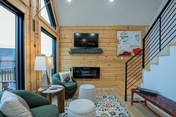 A cozy living room with a green sofa, a small table, a TV mounted on the wall, and a staircase. - The Fives - 22450 Cloud View Luxury Japandi Cabin (Bristol)
