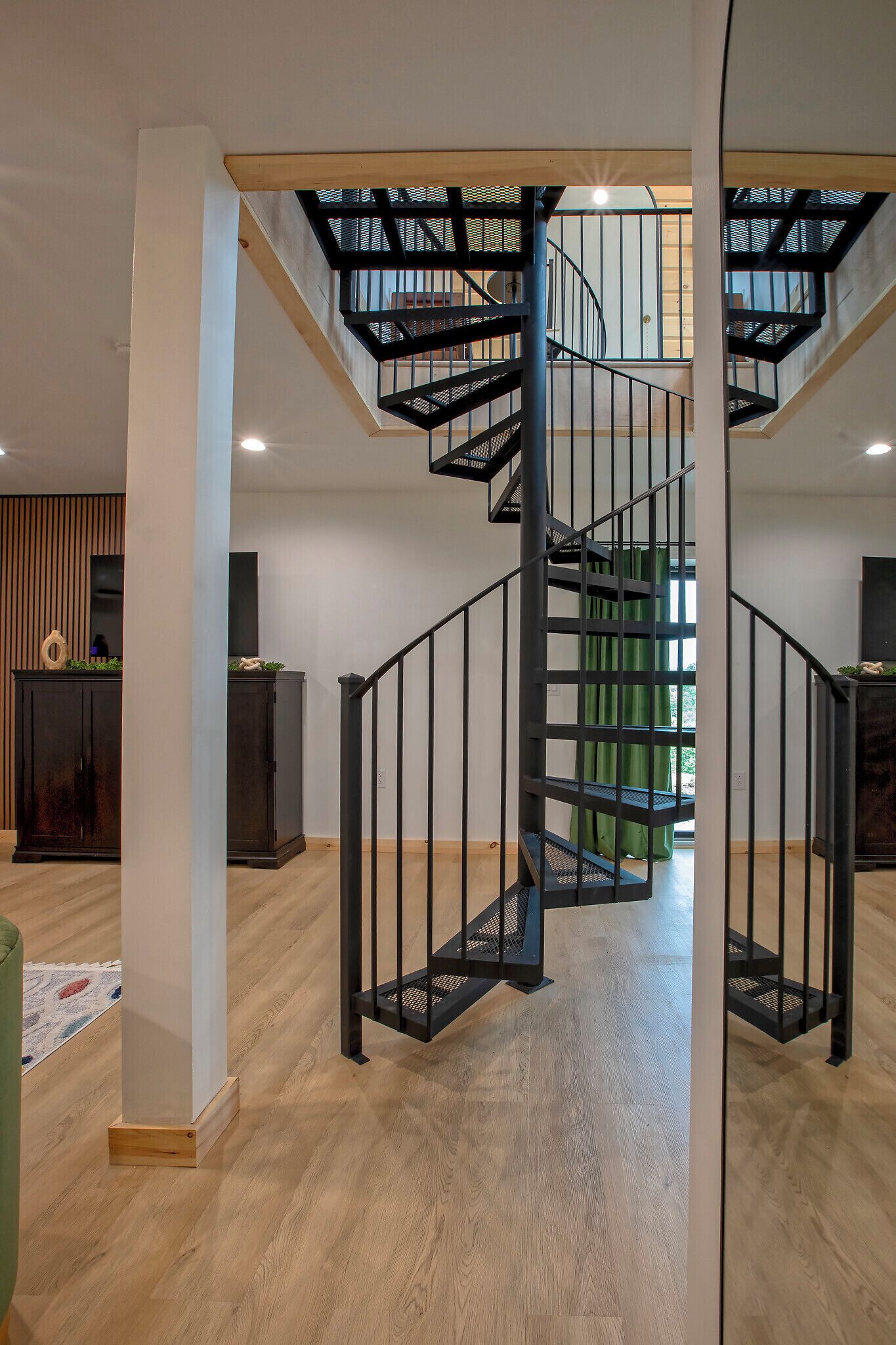Interior moderno com escada em espiral, soalho de madeira e vista para o exterior através de uma janela.
