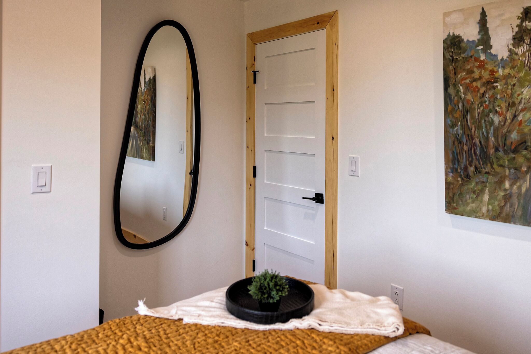 A bedroom with a bed, a mirror, a door, and a painting on the wall.