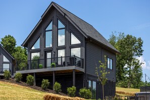 Een modern huis met twee verdiepingen, een balkon, grote ramen en een donkere gevel.