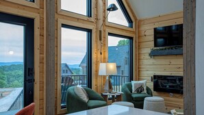 Ein gemütliches Cabin-Interieur mit großen Fenstern, einem an der Wand montierten Fernseher und einem Kamin.