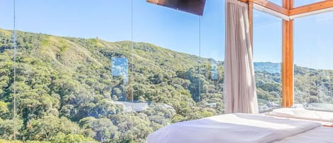 Un dormitorio con un ventanal que da a una ladera boscosa.