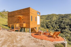 Eine Holzhütte mit Terrasse, Sitzgelegenheiten im Freien und einem malerischen Hügelblick.