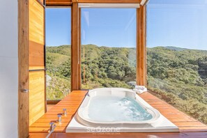 A wooden deck with a hot tub overlooking a forested hillside. - Incrível cabana vista da serra VST021 (Anitapolis)