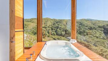 A wooden deck with a hot tub overlooking a forested hillside.