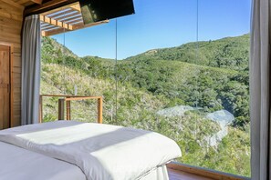 A bedroom with a large window overlooking a mountainous landscape. - Incrível cabana vista da serra VST021 (Anitapolis)