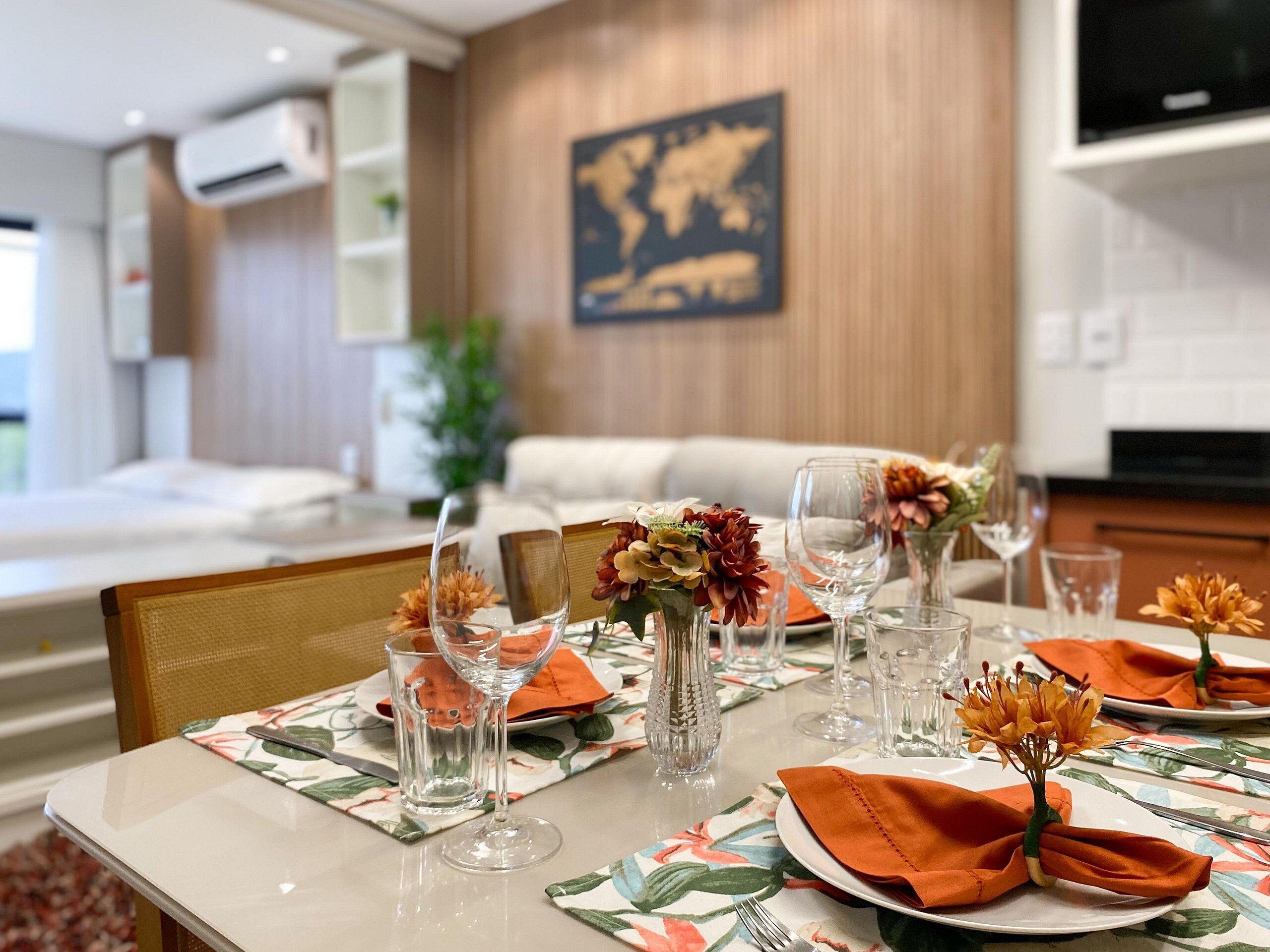 A dining area with a table set for four, featuring floral tablecloths, clear glassware, and orange napkins.