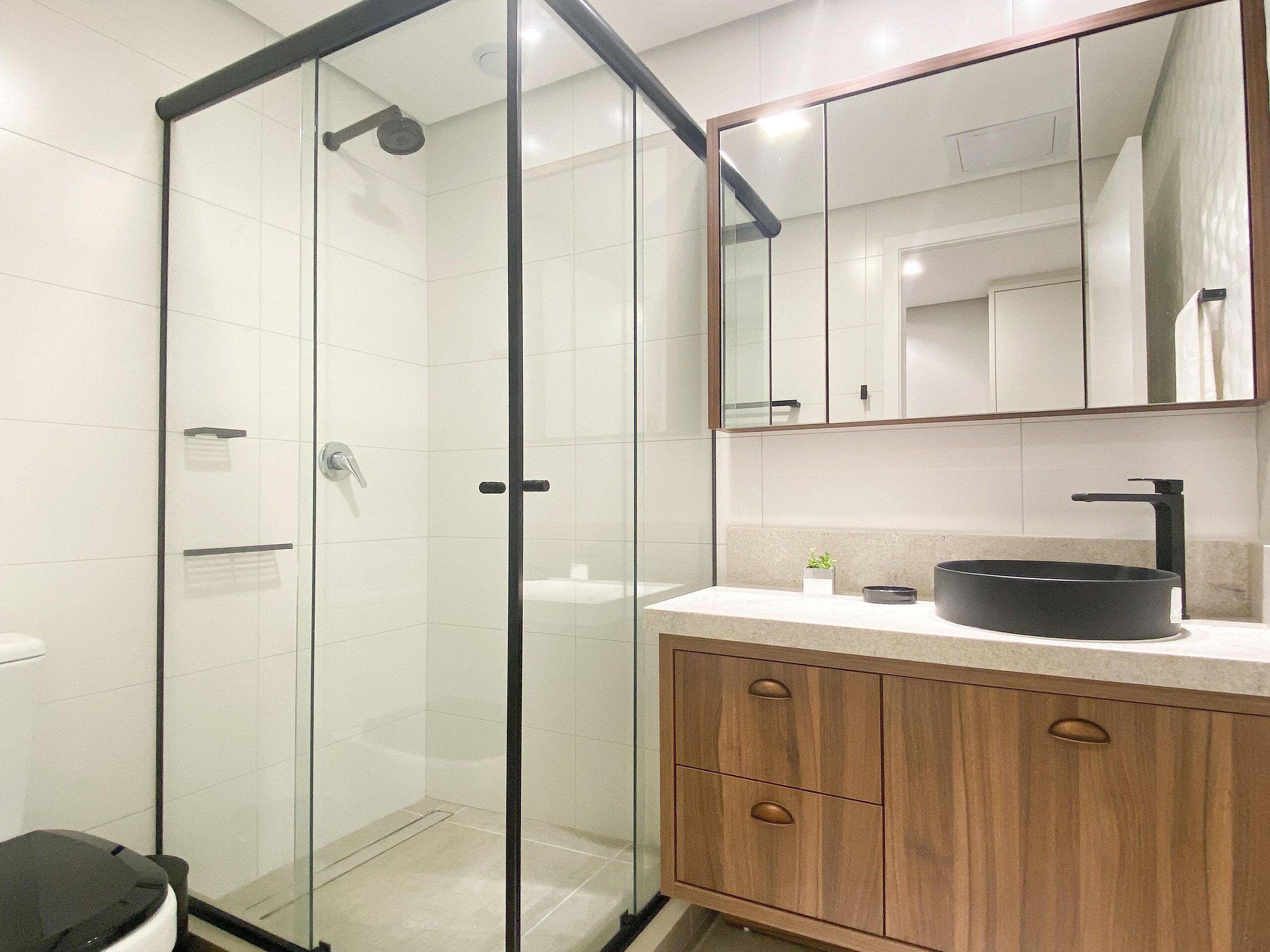 A modern bathroom with a glass-enclosed shower, a wooden vanity with a black sink, and a mirror above the vanity.
